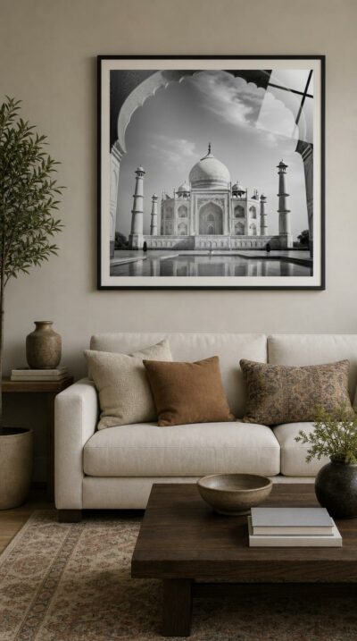 The white marble mausoleum rises beneath a soft sky, framed by a carved Mughal arch and mirrored in still water, in luminous black and white.