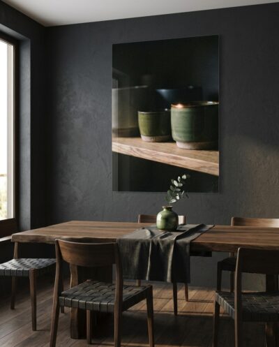 Matte stoneware cups rest on an oak shelf as a single glazed rim gathers the last warm ember of light from the surrounding dark.