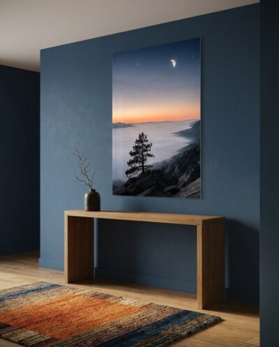 A solitary pine crests a granite ridge as morning's amber light quietly dissolves the lingering night mist beneath a slender crescent moon.
