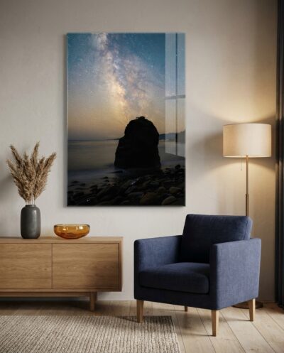 The radiant Milky Way core arcs beside a dark sea stack, casting subtle starlight over quiet waters and smooth coastal stones.