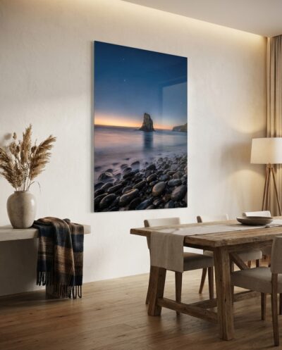 Twilight settles over a solitary sea monolith as long-exposure tides gently wash across dark, glistening coastal stones.